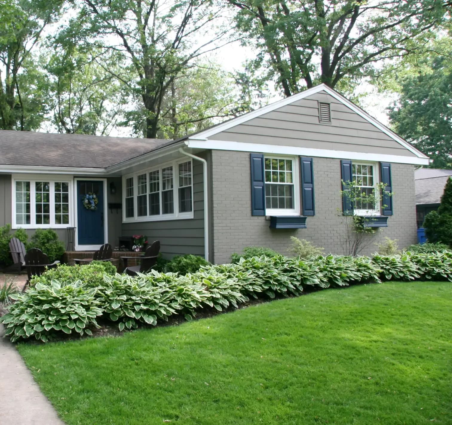House with grey siding and blue window shutters on bright green yard